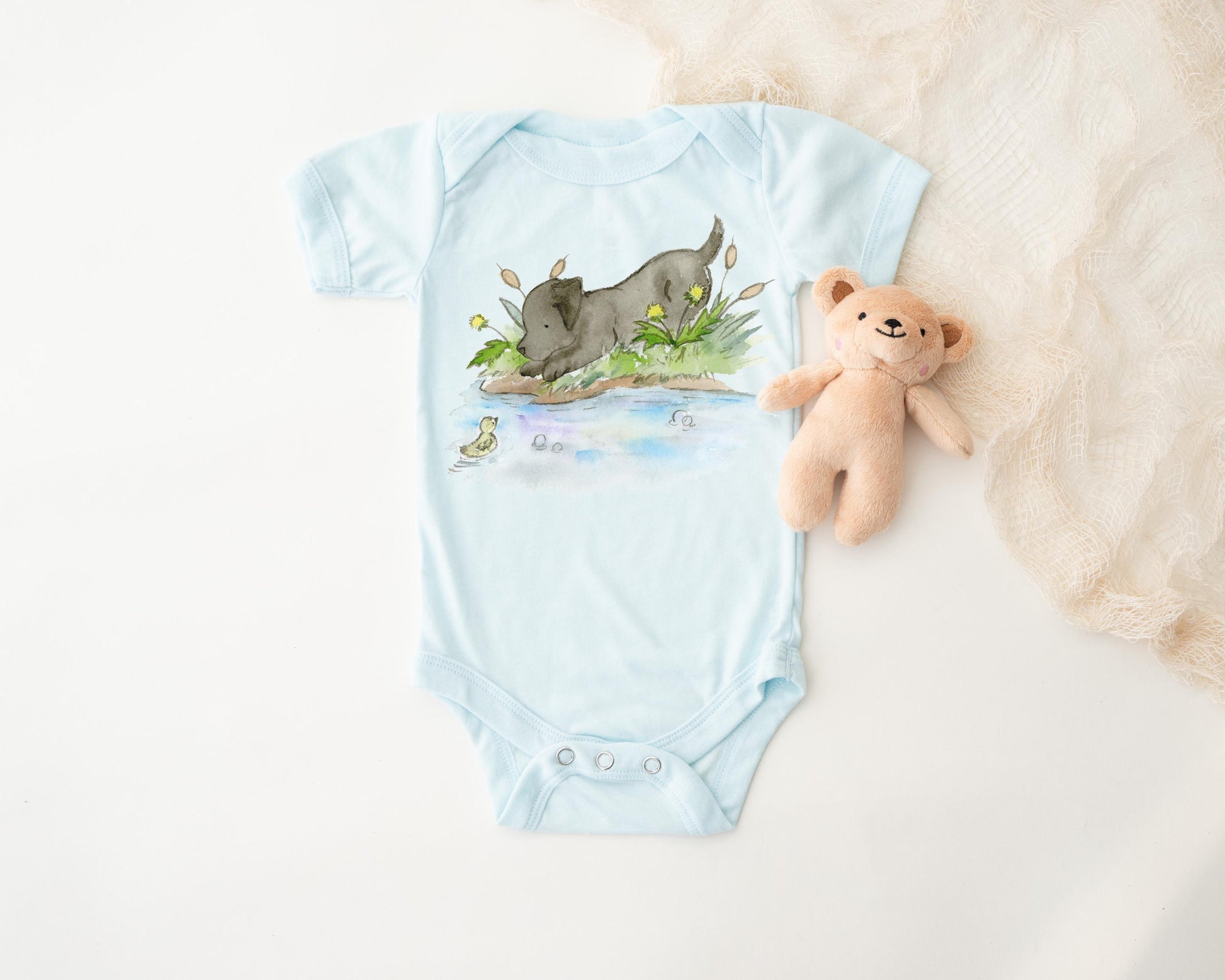 Light blue baby onesie with black lab design on a white surface
