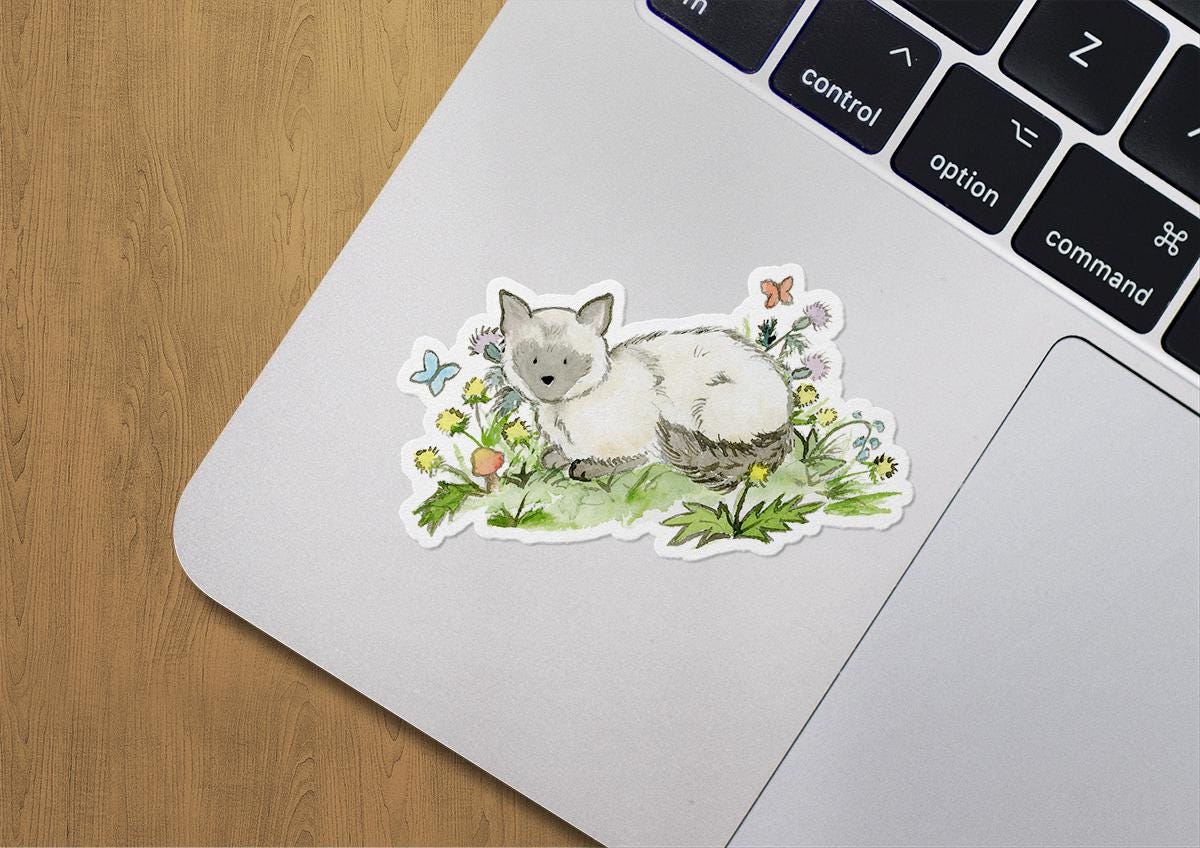 Laptop with a sticker of a cat among flowers on a wooden surface