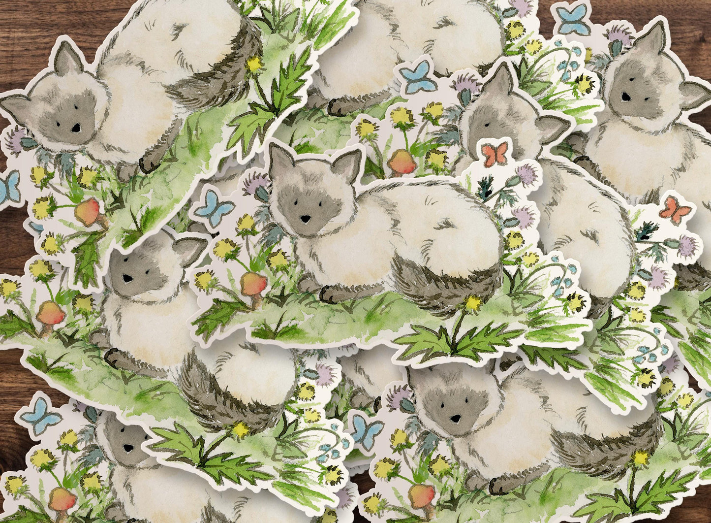 Stickers of a cute siamese cat surrounded by flowers and leaves on a wooden surface.