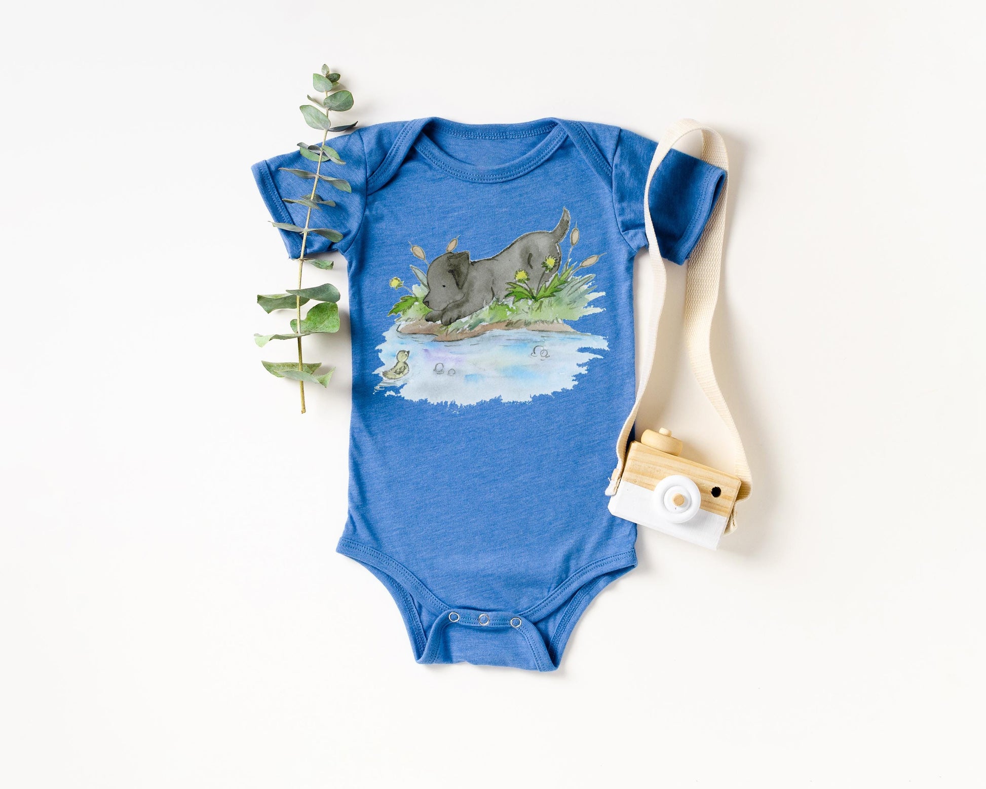 Blue baby onesie with a graphic design of a dog and nature scene on a white background