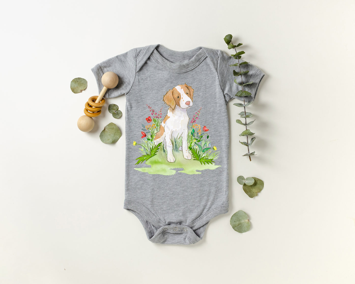 Gray baby onesie with a brittany spaniel dog and floral design on a white background