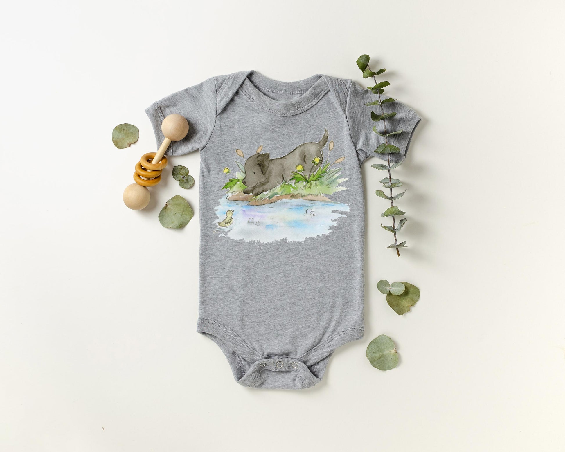 Gray baby onesie with a nature-themed black lab puppy design on a white background