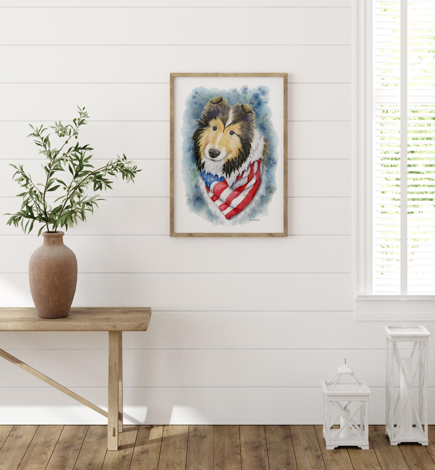 Framed artwork of a sheltie dog with an American flag design on a wall in a room with a wooden table and vase.