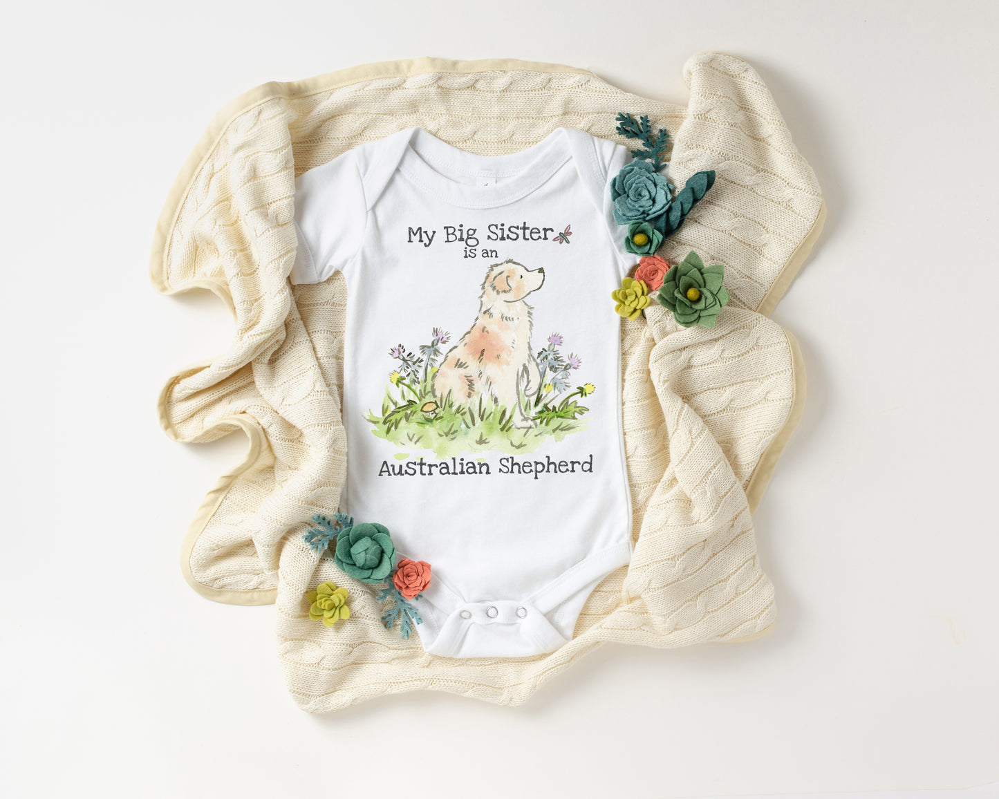 Baby onesie with Australian Shepherd design and text, surrounded by decorative flowers on a white background