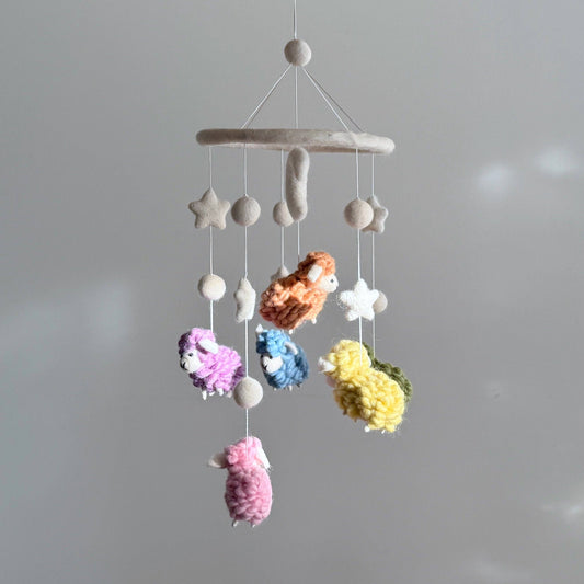 Colorful baby mobile with stars and lambs hanging against a gray background