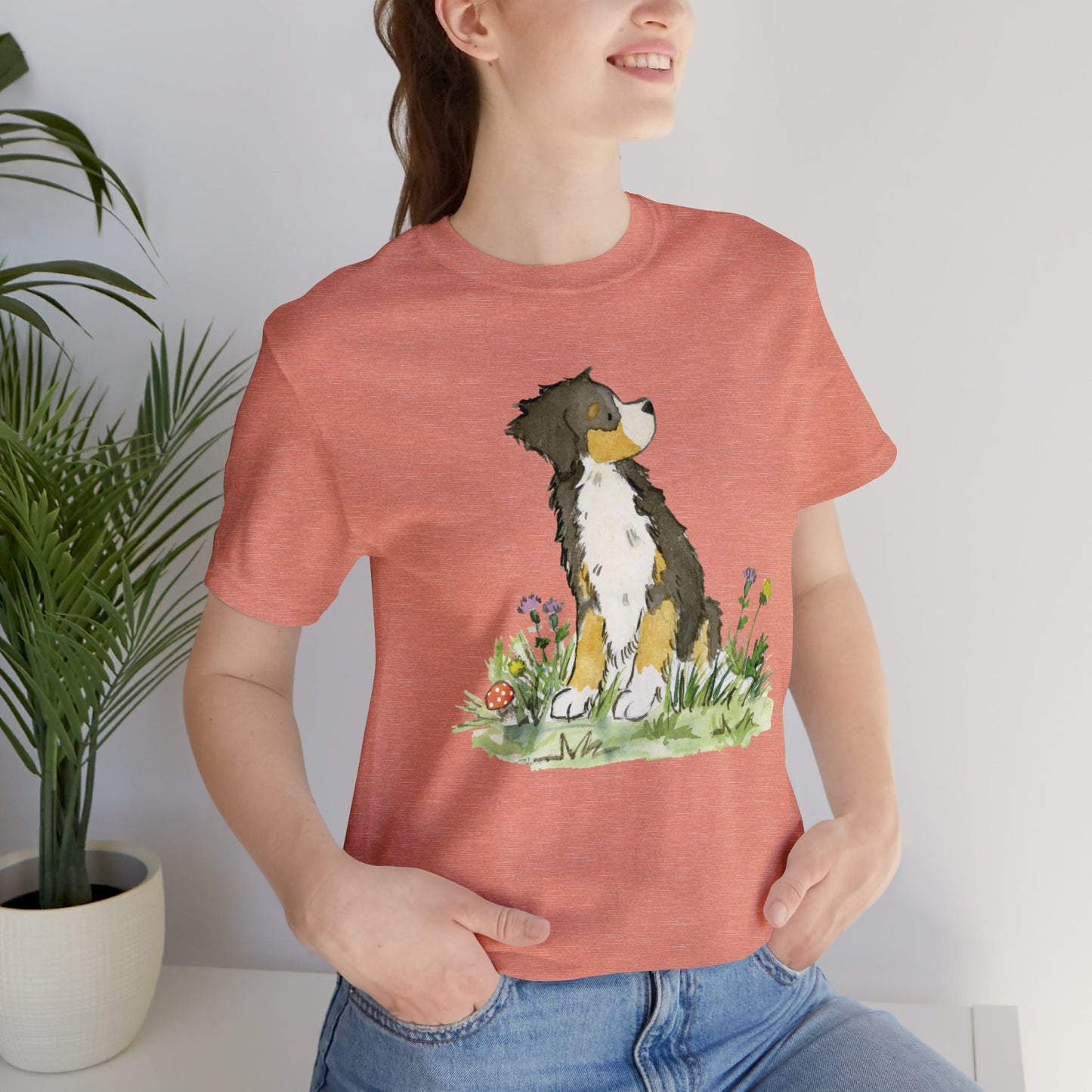 Woman wearing sunset orange pink tee with cute Bernese mountain dog artwork on it.