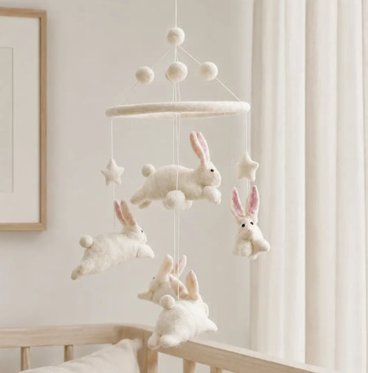 A soft white felt baby mobile with bunny and star shapes hanging in front of a crib in a bright nursery.