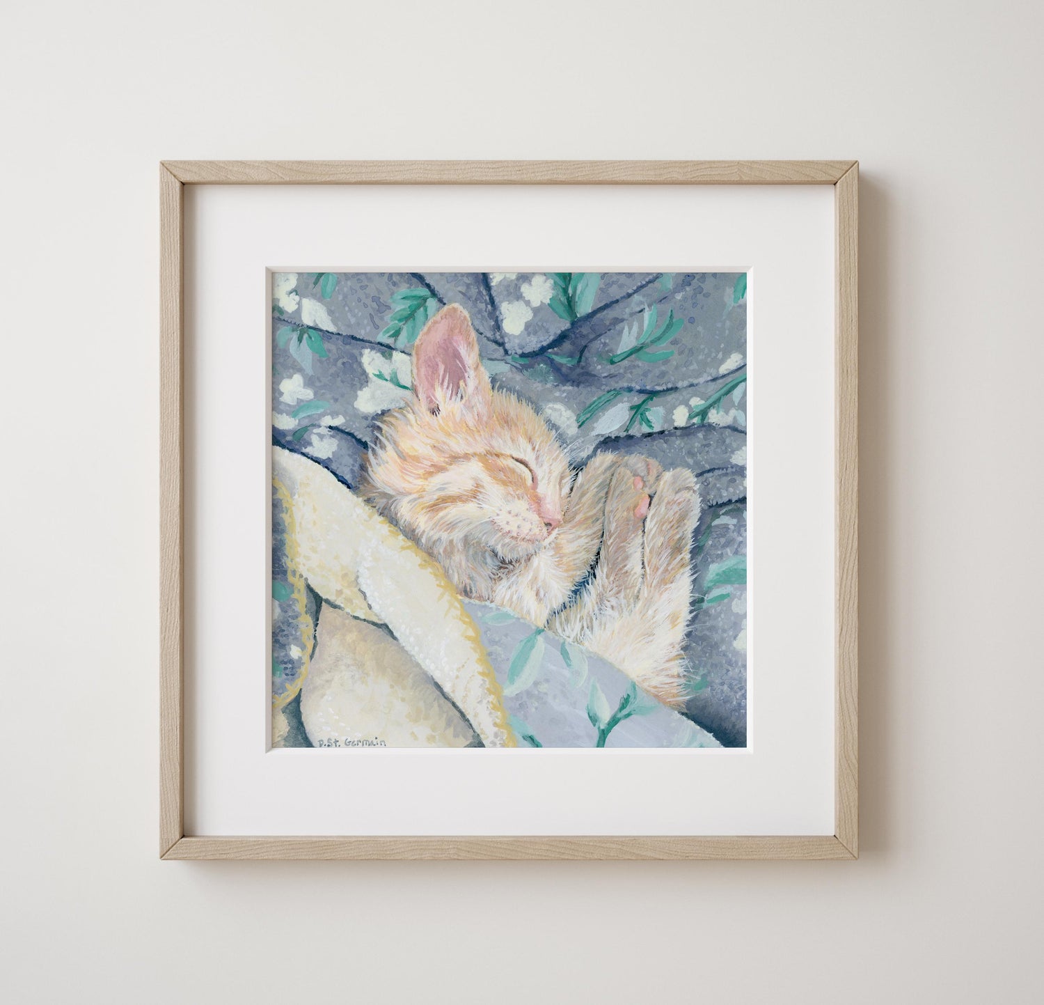 Framed gouache painting of an orange ginger kitten taking a nap in a gray and teal floral blanket.