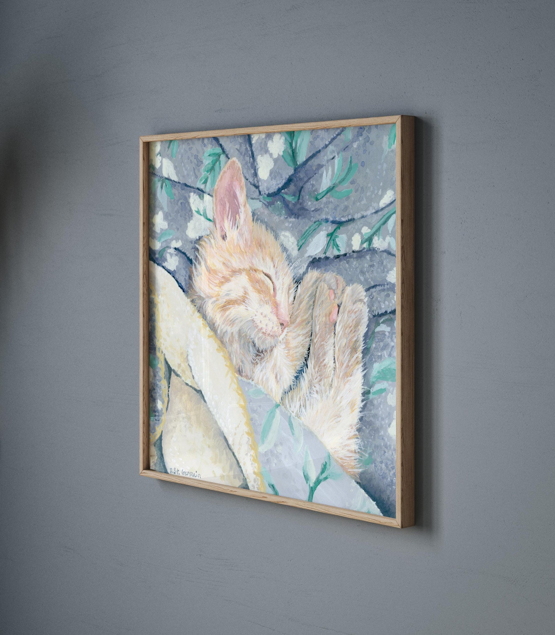 Framed gouache painting of an orange ginger kitten taking a nap in a gray and teal floral blanket.