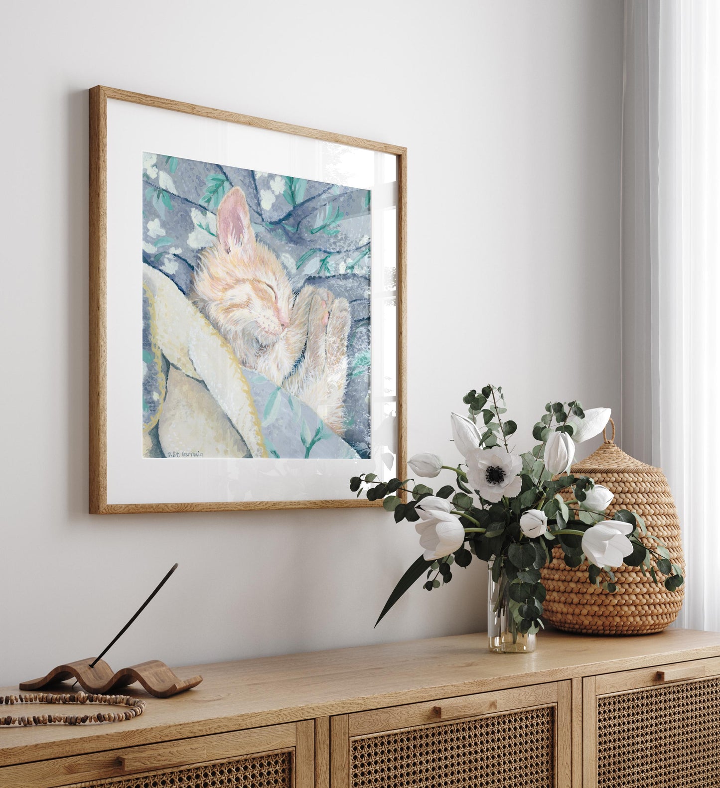 Framed gouache painting of an orange ginger kitten taking a nap in a gray and teal floral blanket.