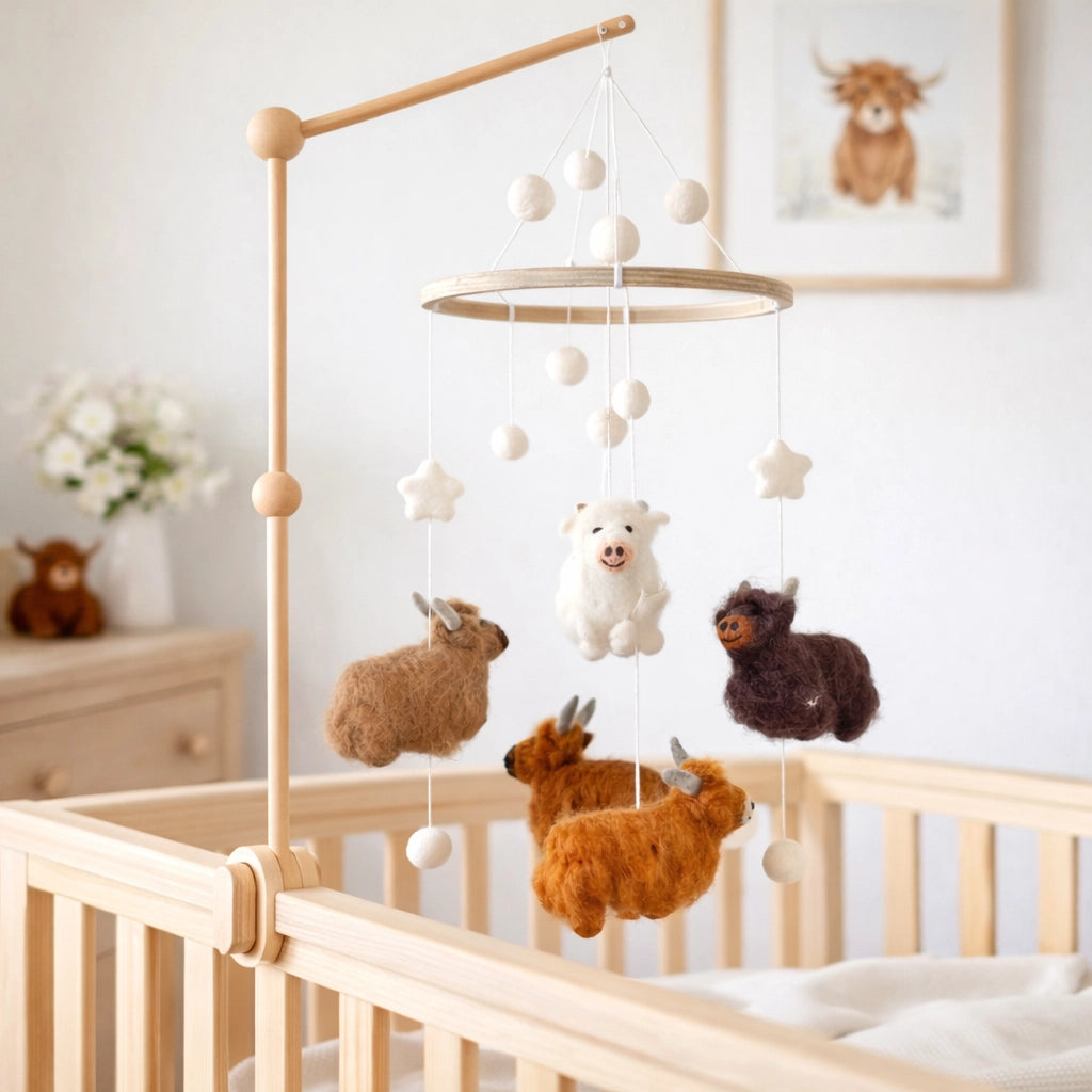 Baby crib with a mobile featuring stuffed wool highland cows in a nursery setting.