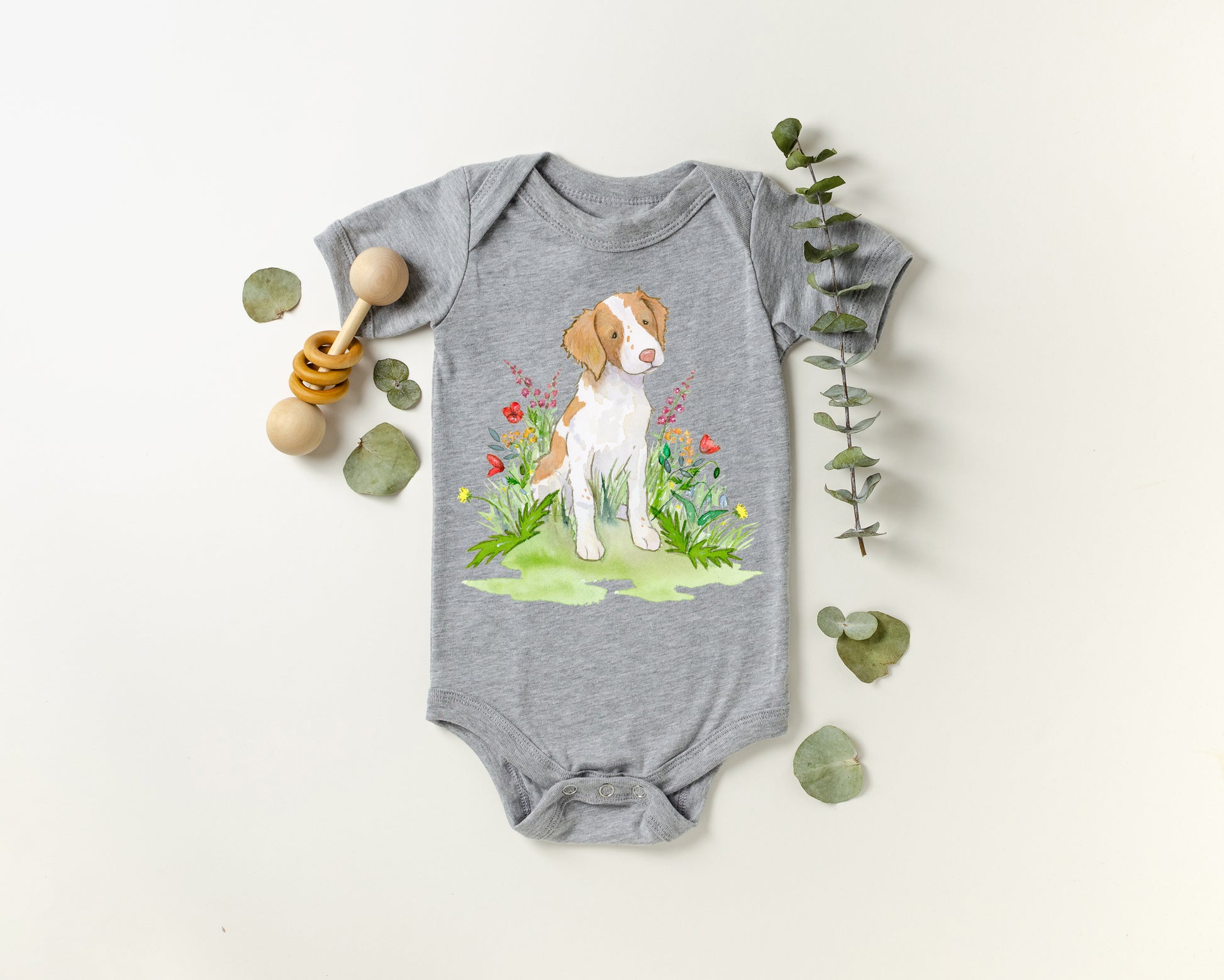 Gray baby onesie with a brittany spaniel dog and floral design on a white background