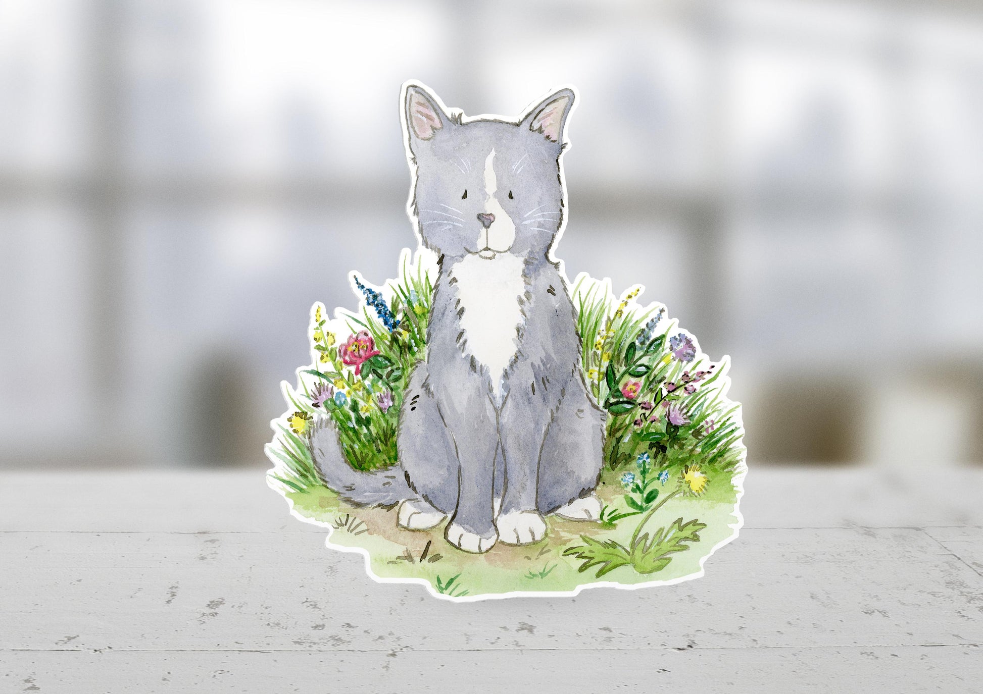 Gray and white kitten sitting in a patch of colorful flowers sticker.