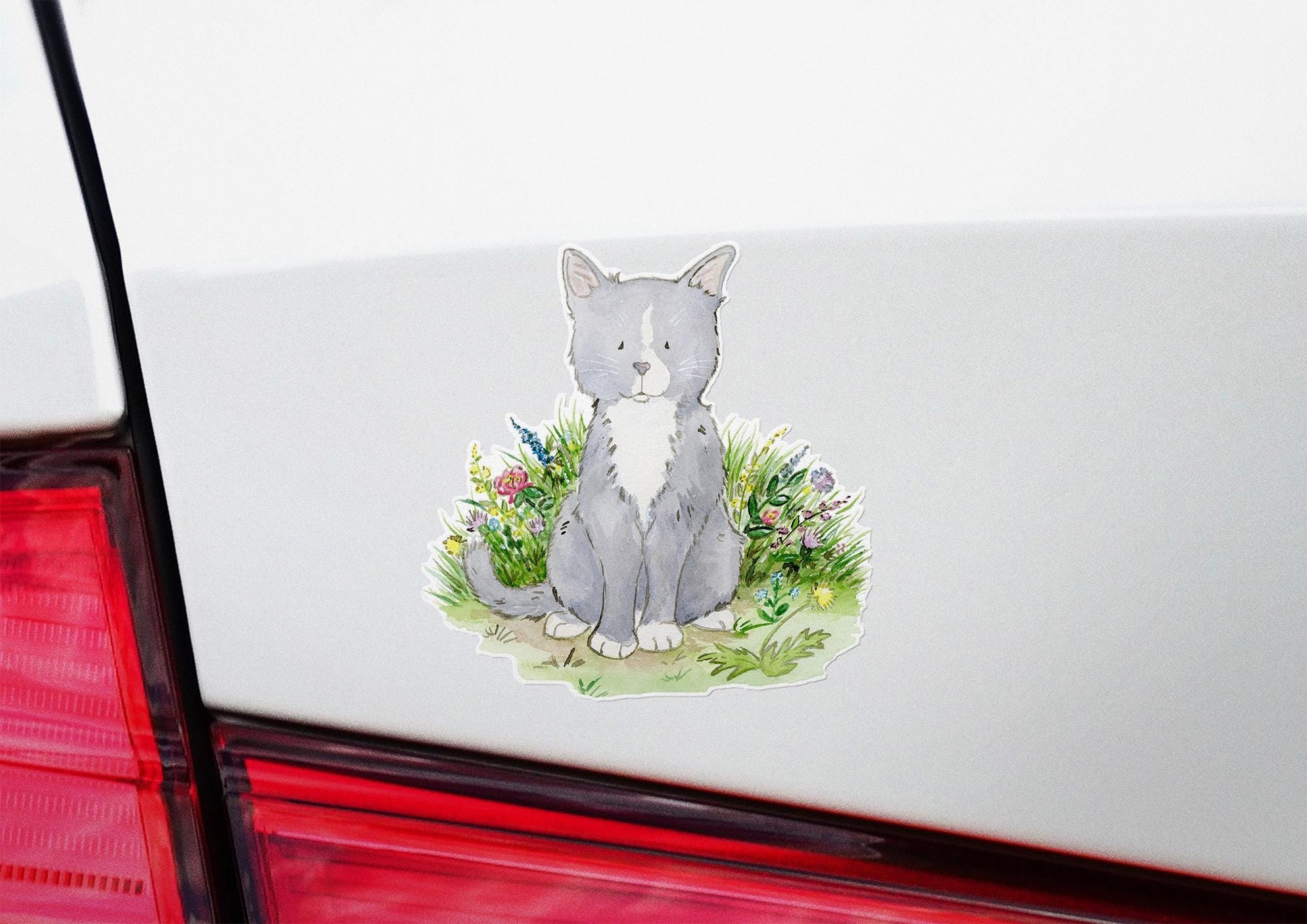 Gray and white kitten sitting in a patch of colorful flowers sticker.