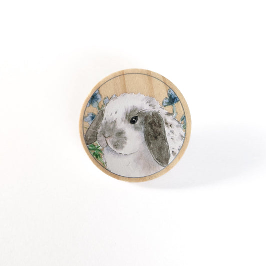 Round wooden pin with a gray and white spotted holland lop bunny and flowers on it.