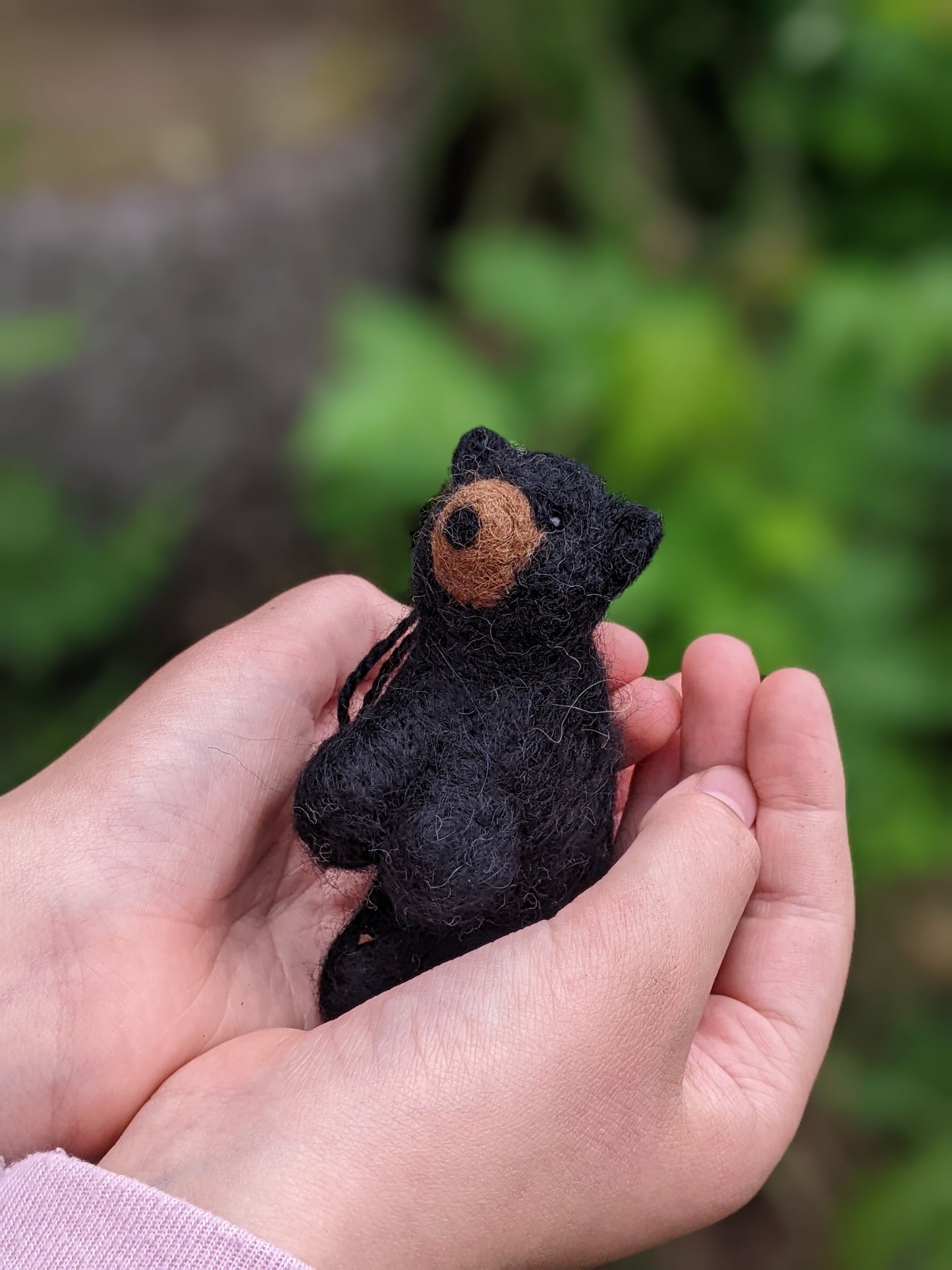 needle felted wool black bear cub sculpture held in a child's hands