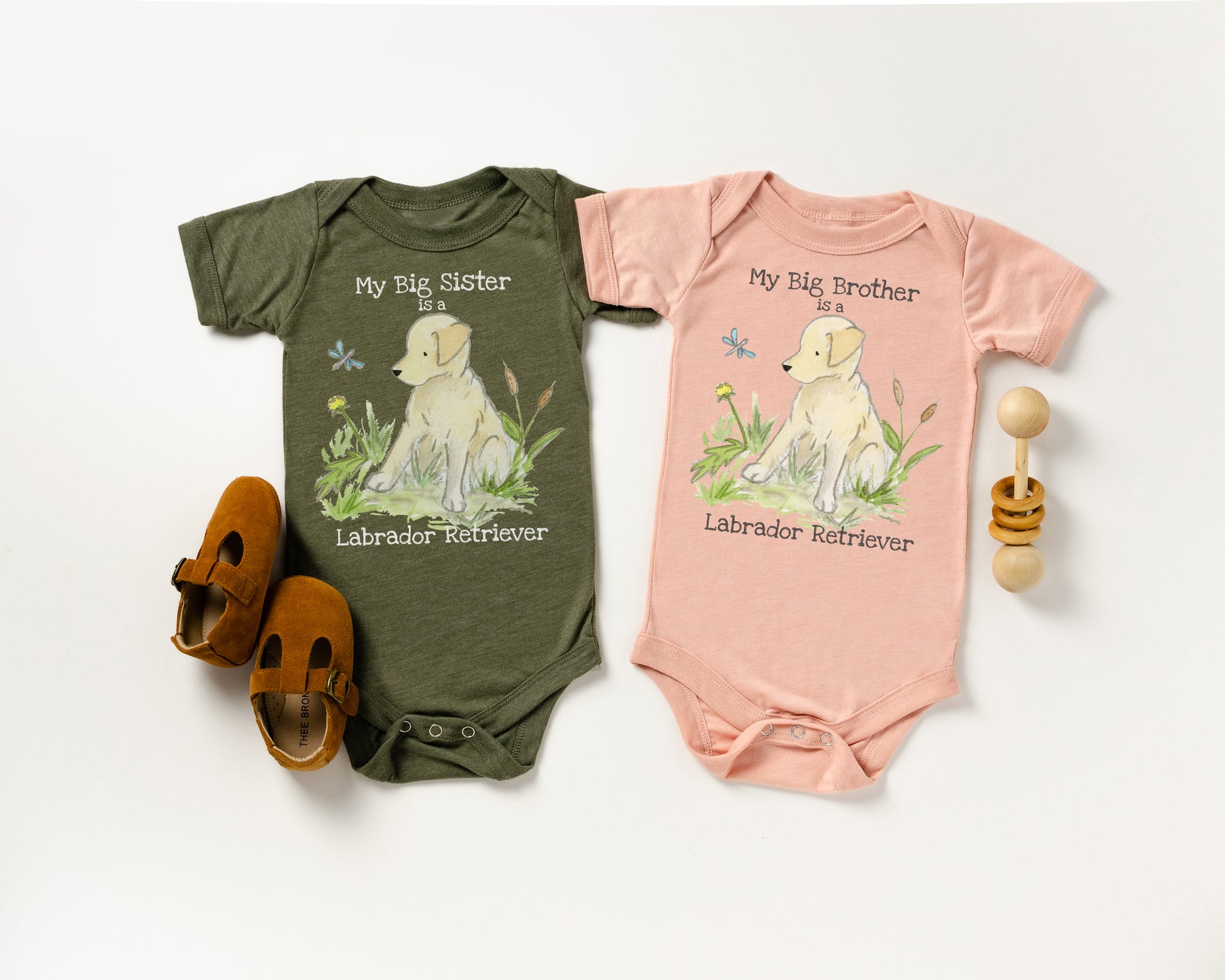 Two baby onesies with Labrador Retriever illustrations and shoes on a white background
