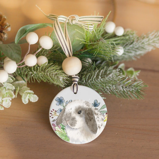 White ceramic ornament with watercolor painting of grey and white spotted Holland Lop bunny rabbit and colorful wildflowers.