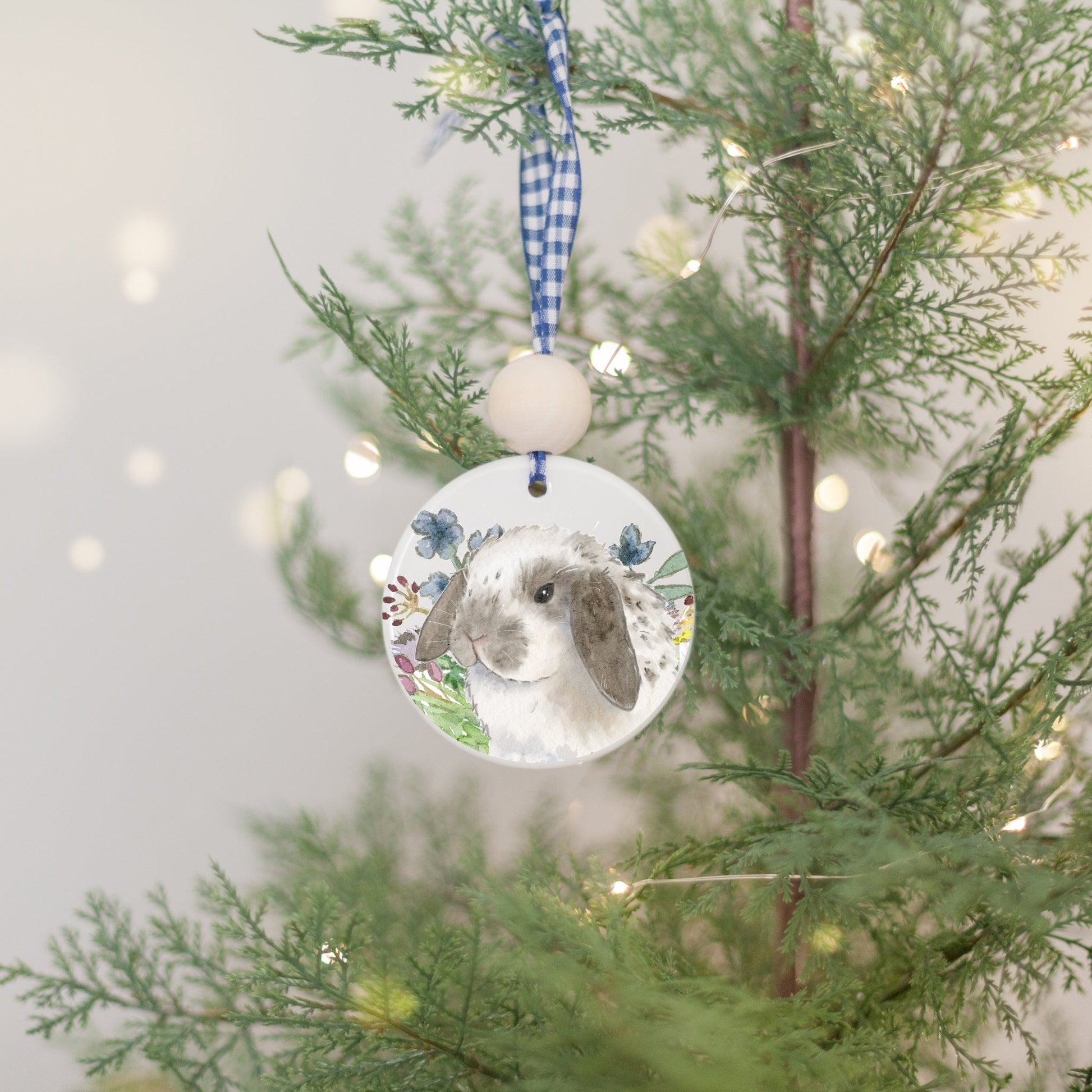 White ceramic ornament with watercolor painting of grey and white spotted Holland Lop bunny rabbit and colorful wildflowers.