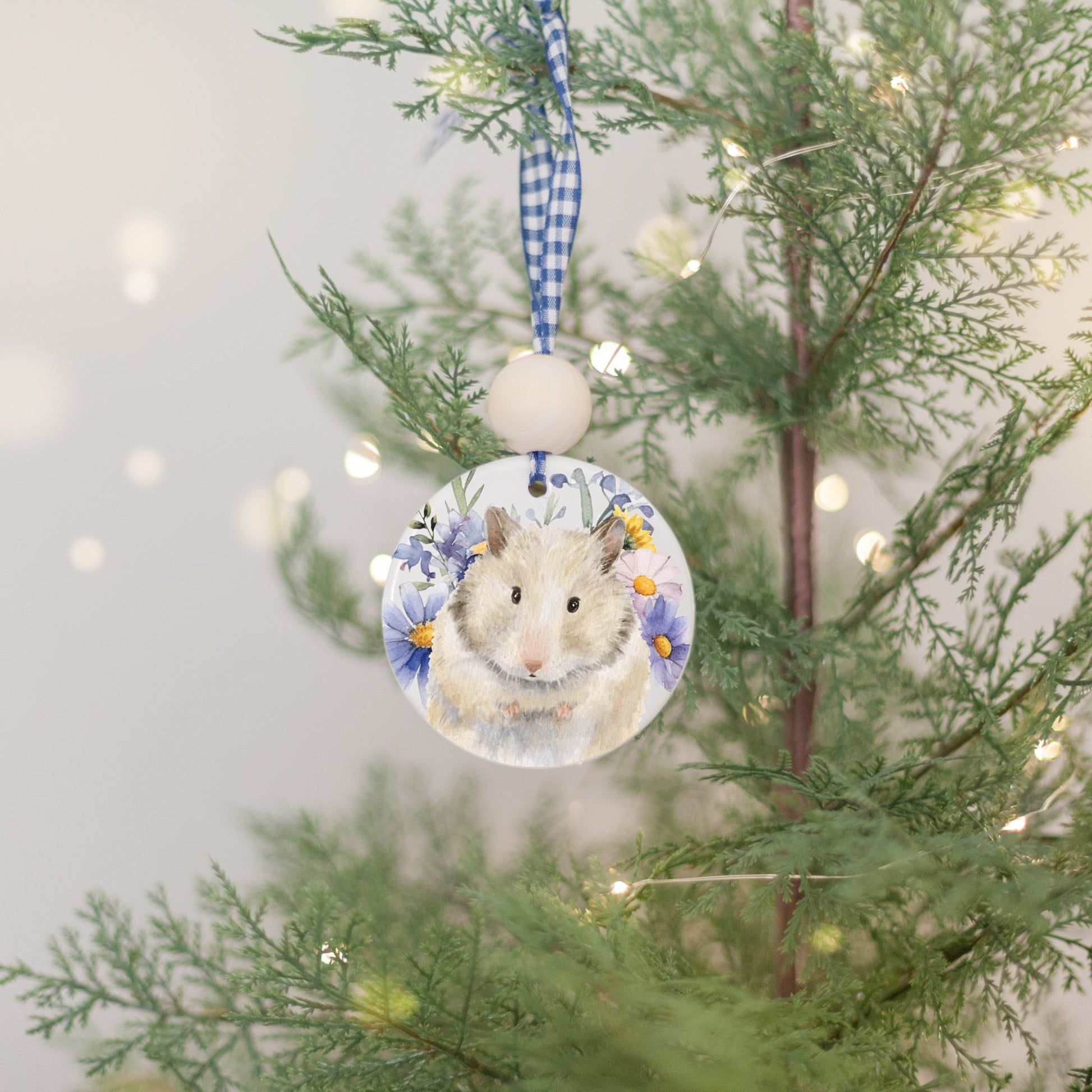 ceramic ornament with watercolor painting of cream and brown hamster and wildflowers hanging on Christmas tree
