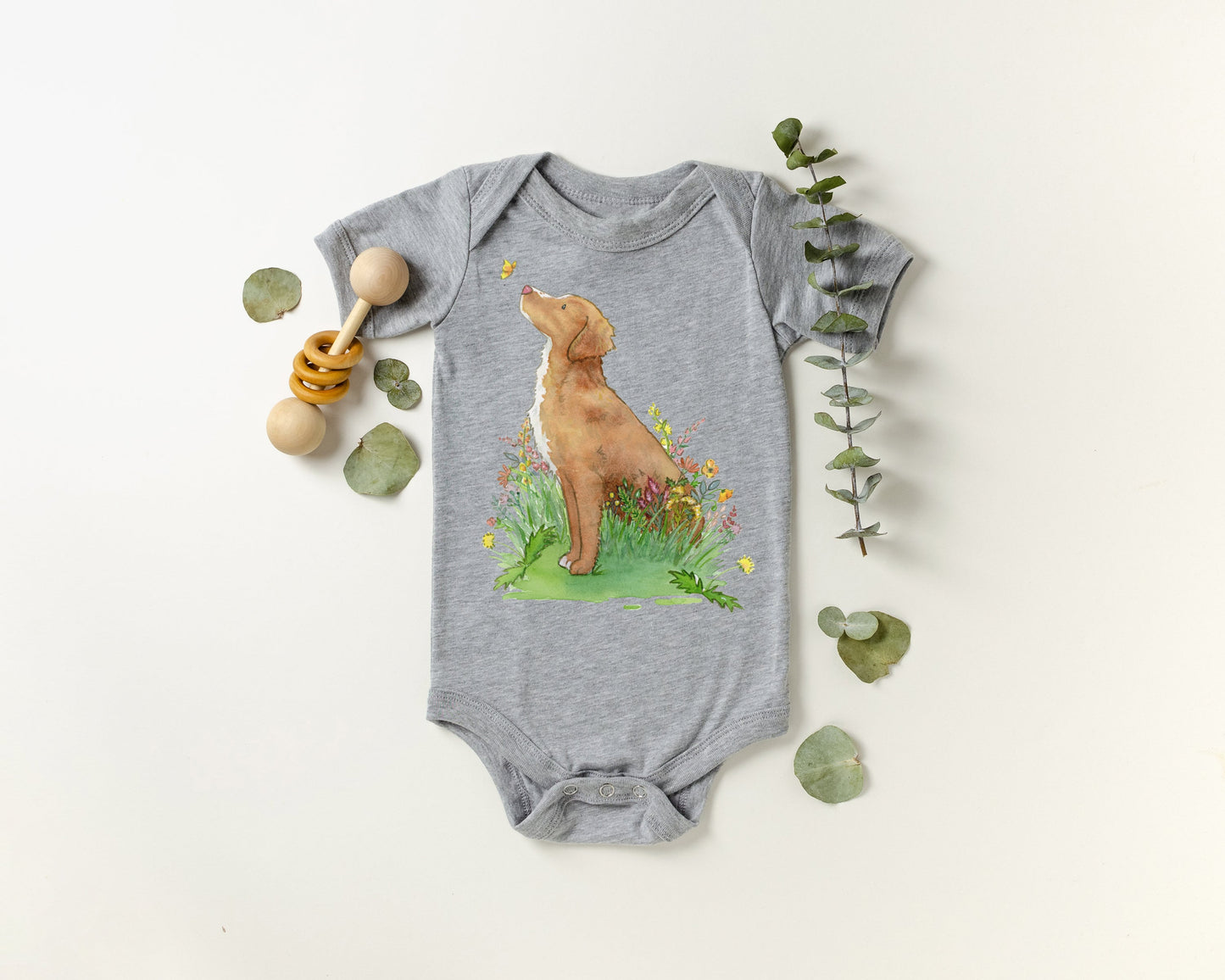 Baby one-piece bodysuit with cute artwork of a Nova Scotia Duck Tolling Retriever looking at a butterfly on it.